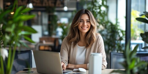 Wall Mural - A woman is sitting at a table with a laptop and a cup. She is smiling and she is happy