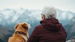 © Vuvimages - An elderly woman clad in a maroon jacket gazes toward mountains, alongside her loyal dog adorned with beads, symbolizing companionship and tranquility.