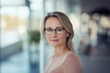 © GustavsMD - Professional woman wearing glasses, confidently posing in a bright, modern office environment with soft natural lighting.
