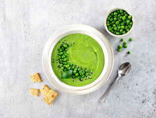 Green pea cream soup with crackers on a gray table. Top view.