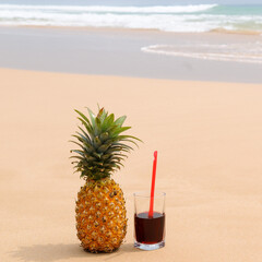 Ripe pineapple and juice in a glass on a sandy beach.