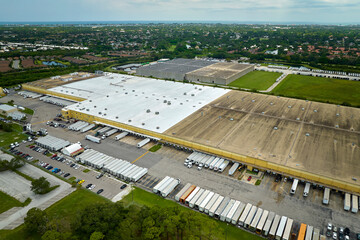 High angle view of big commercial shipping center with many freight trucks unloading and uploading goods for further distribution. Global economy concept