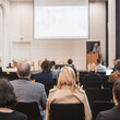 © kasto - Speaker giving a talk in conference hall at business event. Rear view of unrecognizable people in audience at the conference hall. Business and entrepreneurship concept