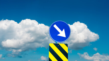 A circular traffic sign with a white arrow pointing down-right, mounted on a striped black and yellow post, set against a sky with scattered clouds.