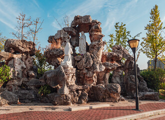 A serene view of a rock formation with two statues nestled in a peaceful park during daylight hours.