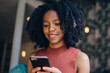 © BullRun - Positive black hipster girl typing text message for sending to friend connected to wifi internet on cellular phone, happy female teenager playing online games on cellphone during leisure time