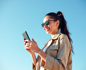 A woman is typing and smiling on her phone against a blue sky background