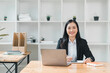 © PRIME STOCK LAB - professional woman is sitting at desk in modern office environment, smiling confidently while working on laptop. background features shelves with plants and organized office supplies, creating