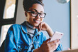 © BullRun - Portrait of positive dark skinned female teenager smiling at camera while waiting for text message from friend during online chatting via cellular gadget, concept of technology and communication