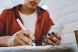 © BullRun - Selective focus on female hand holding modern cellular phone in hands and using 4g wireless internet for making research of information for school homework and making notes in textbook for education