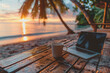 © PHAISITSAWAN - A laptop and a coffee cup are on the table with a sunset beach view in the background.