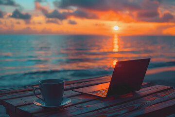 A laptop and a coffee cup are on the table with a sunset beach view in the background.