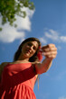 © Connect Images - Woman in a red dress holding a flower against a blue sky with clouds.