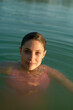 © Connect Images - Woman bathing in a body of water with her hair pulled back and sunlight highlighting her face.