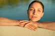 © Connect Images - Woman relaxing in a swimming pool at sunset with water droplets on her face and arms rested on pool edge.