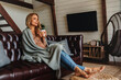 © InsideCreativeHouse - Full length of dreaming middle aged woman sitting in living room with cup of coffee or tea enjoying under blanket