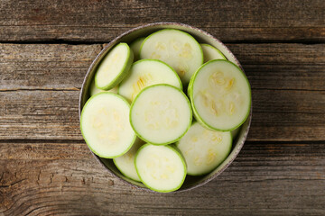 Fresh cut zucchinis in bowl on wooden table, top view