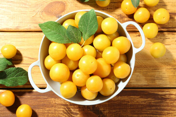 Poster - Tasty ripe plums and leaves in colander on wooden table, flat lay