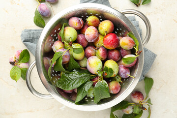 Sticker - Ripe plums and leaves in colander on light table, flat lay