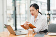 © PRIME STOCK LAB - focused woman in white shirt is working at modern office desk, using laptop while holding notebook. She appears engaged and thoughtful, surrounded by coffee cup and tablet.
