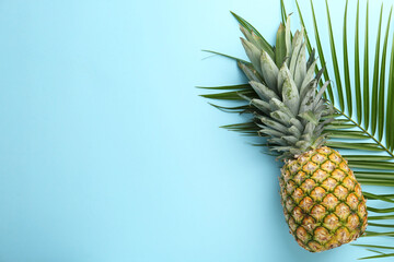 Fresh ripe pineapple and palm leaf on light blue background, top view. Space for text