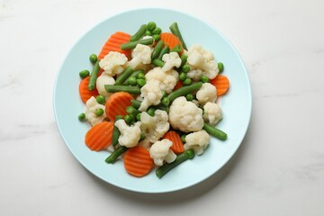 Tasty cooked cauliflower with green peas, string beans and carrot slices on white marble table, top view