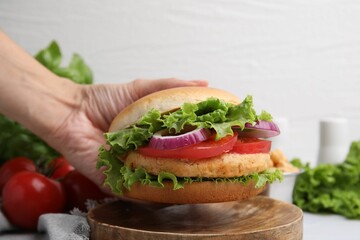 Woman holding vegetarian burger with chickpea cutlet at table, closeup