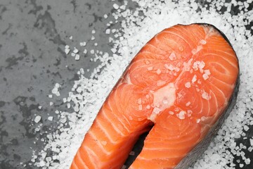 Fresh raw salmon steak with salt on dark textured table, above view. Space for text