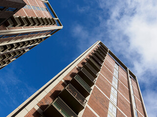 Low-angle view of two tall apartment buildings against a clear blue sky.