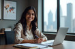 © OtonaLechuza - An Indian female economist smiles while working on her laptop, surrounded by charts and graphs on the walls. Stacks of reports are neatly placed on her desk