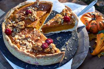 top view of pumpkin pie on a black tray stands on a wooden table with pumpkins and fall leaves