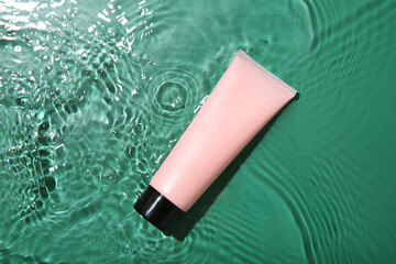 Poster - Cosmetic product. Tube with cream in water on green background, top view