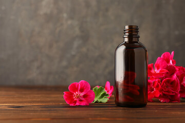 Wall Mural - Geranium essential oil in bottle and beautiful flowers on wooden table, space for text