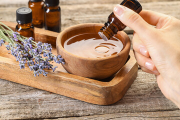 Wall Mural - Woman dripping essential oil into bowl with water at wooden table, closeup