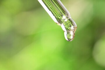 Wall Mural - Essential oil dripping from pipette against blurred green background, closeup. Space for text