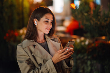 Woman wearing earbuds listening to music on smartphone at night