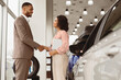 © Prostock-studio - Buying Car Concept. Afro Businessman Handshaking With Manager Girl Standing Near Auto In Automobile Dealership Shop. Free Space