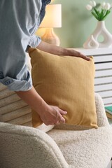 Poster - Woman putting soft pillow onto light armchair in living room, closeup