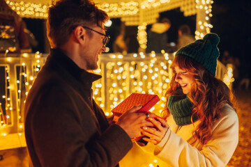 Wall Mural - A happy girl receiving christmas present on street and looking at it.