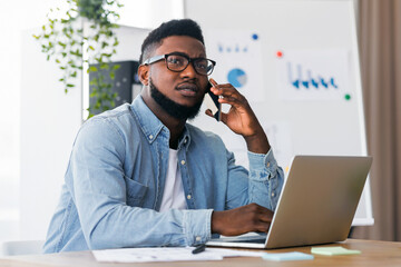 Poster - Young african american manager working on laptop and talking on phone with concerned face expression, having hard day at work