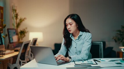 Wall Mural - Young professional woman working late in the office. She is focused on her work but eventually becomes stressed and rubs her temples