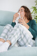 © Lucia PSV - A young woman is very ill, lying on the sofa at home. She has a fever and flu. She feels tired, has muscle fatigue and has a runny nose. She has to take medication that she doesn't like at all and dri
