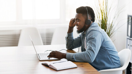 Wall Mural - Customer support concept. Black millennial manager with headset using laptop in office, solving client's issue.