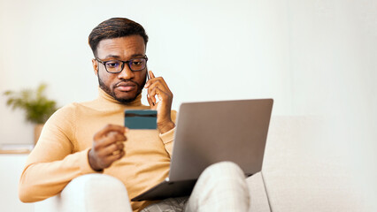 Aufkleber - Online Shopping Problems. Afro Guy Calling By Phone Using Credit Card And Laptop Sitting On Sofa Indoor. Selective Focus