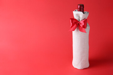 Wall Mural - Wine bottle in burlap bag with satin bow on red background. Space for text