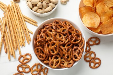 Delicious pretzel crackers and other snacks on white table, flat lay