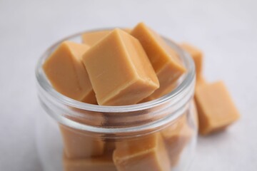 Canvas Print - Tasty sweet caramel candies in glass jar on light table, closeup