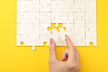 Wall Mural - Woman solving white puzzle on yellow background, closeup