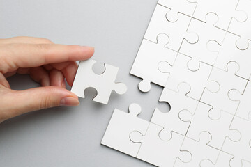 Poster - Woman solving white puzzle on light grey background, top view