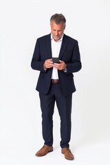 Wall Mural - Happy business man of middle age wearing suit in formal shoes using phone standing isolated on white background. Busy mature businessman with smartphone in hands looking advertising mobile services.